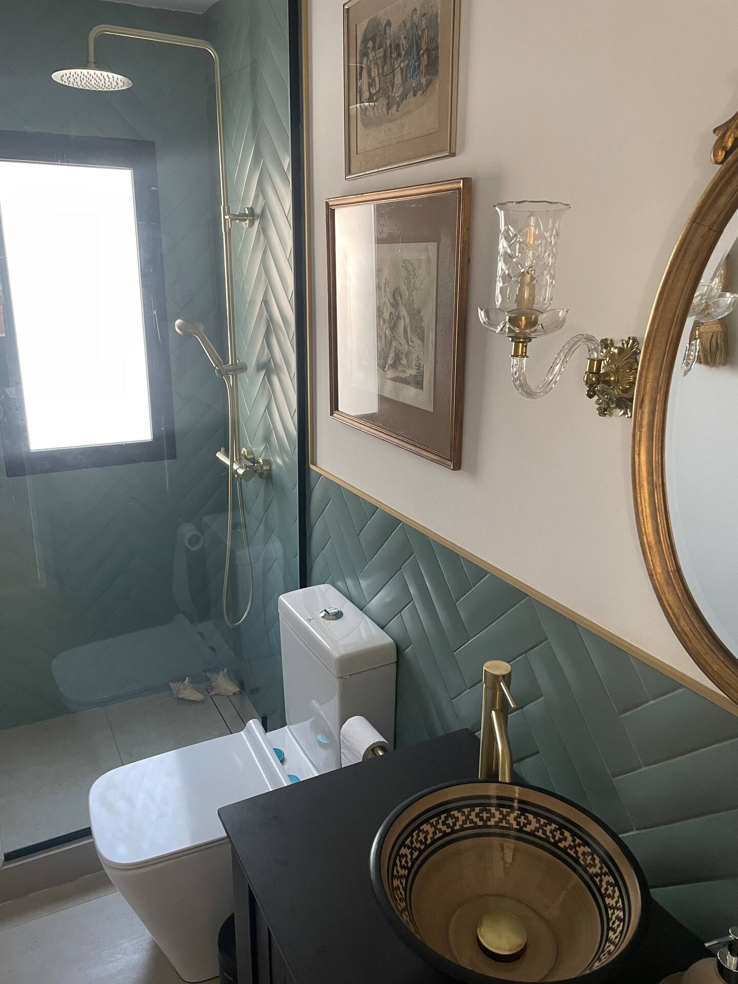 Bathroom with green herringbone tiles, brass shower and ornate mirror