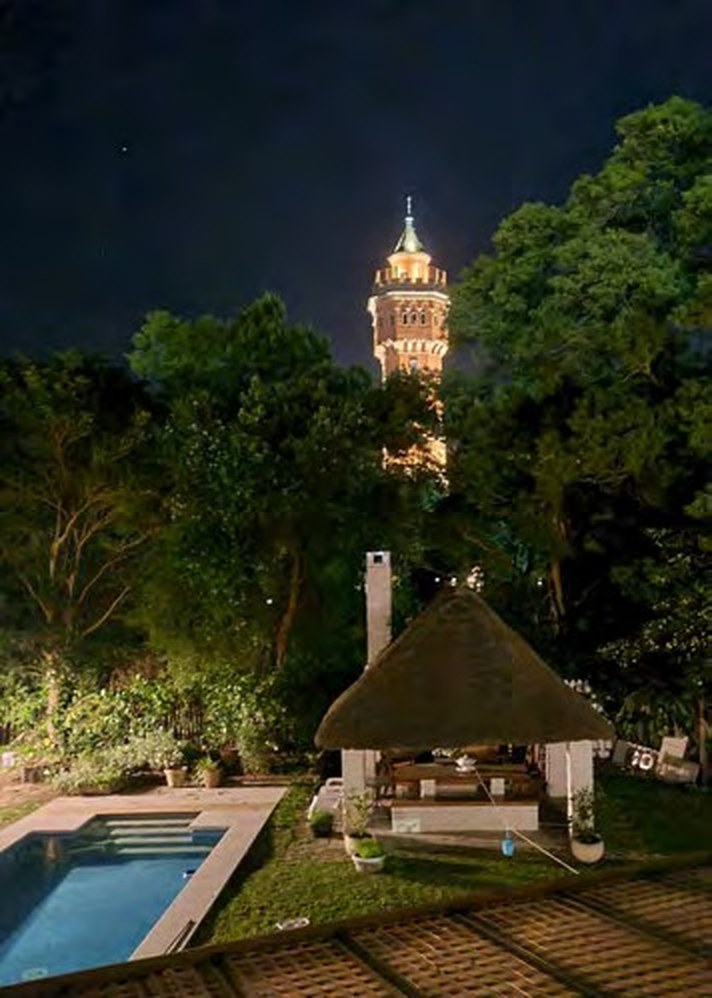 Garden and pool at night with a lit tower beyond the trees